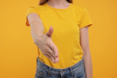 Woman welcoming and offering handshake on yellow background, closeup