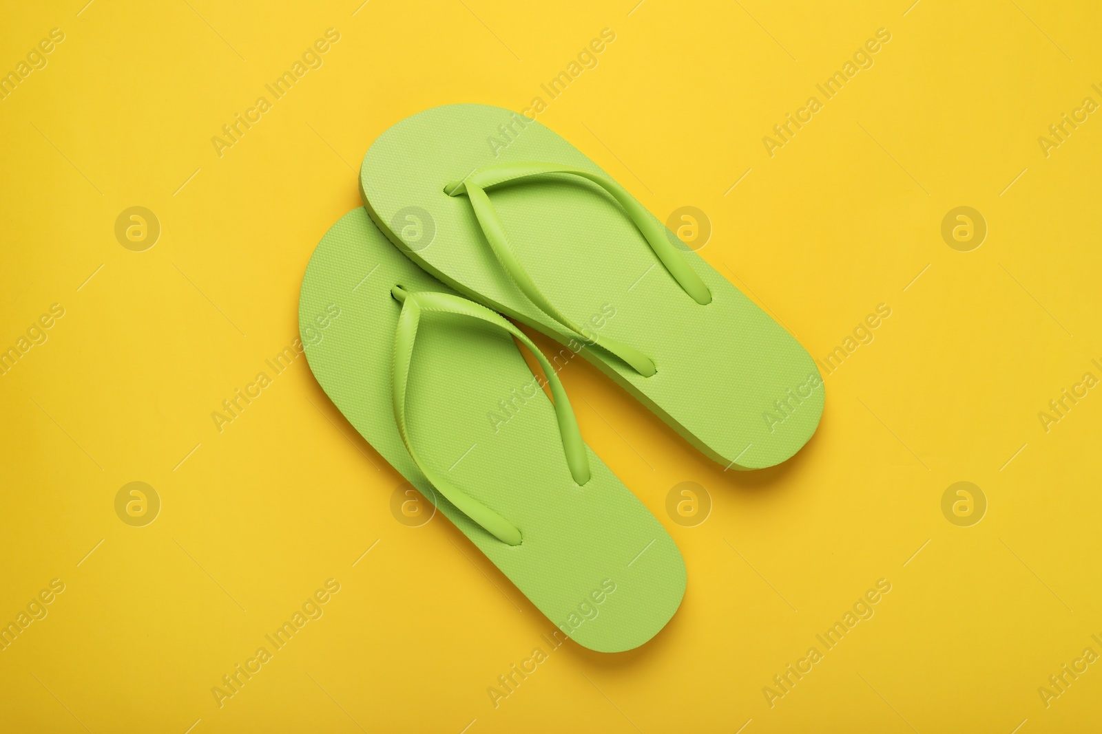 Photo of Stylish light green flip flops on yellow background, top view