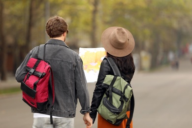 Photo of Couple of travelers with backpacks on city street, back view