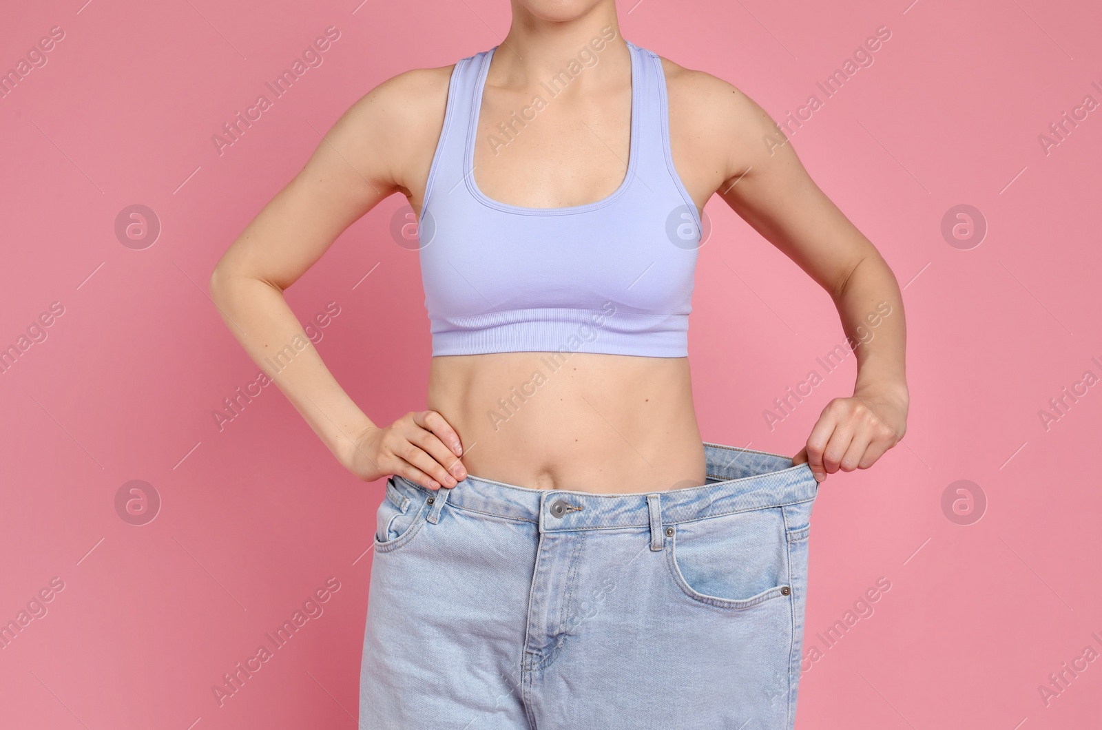 Photo of Woman in big jeans showing her slim body on pink background, closeup