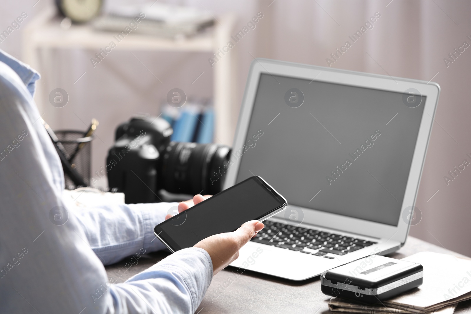 Photo of Journalist with smartphone working at table in office, closeup