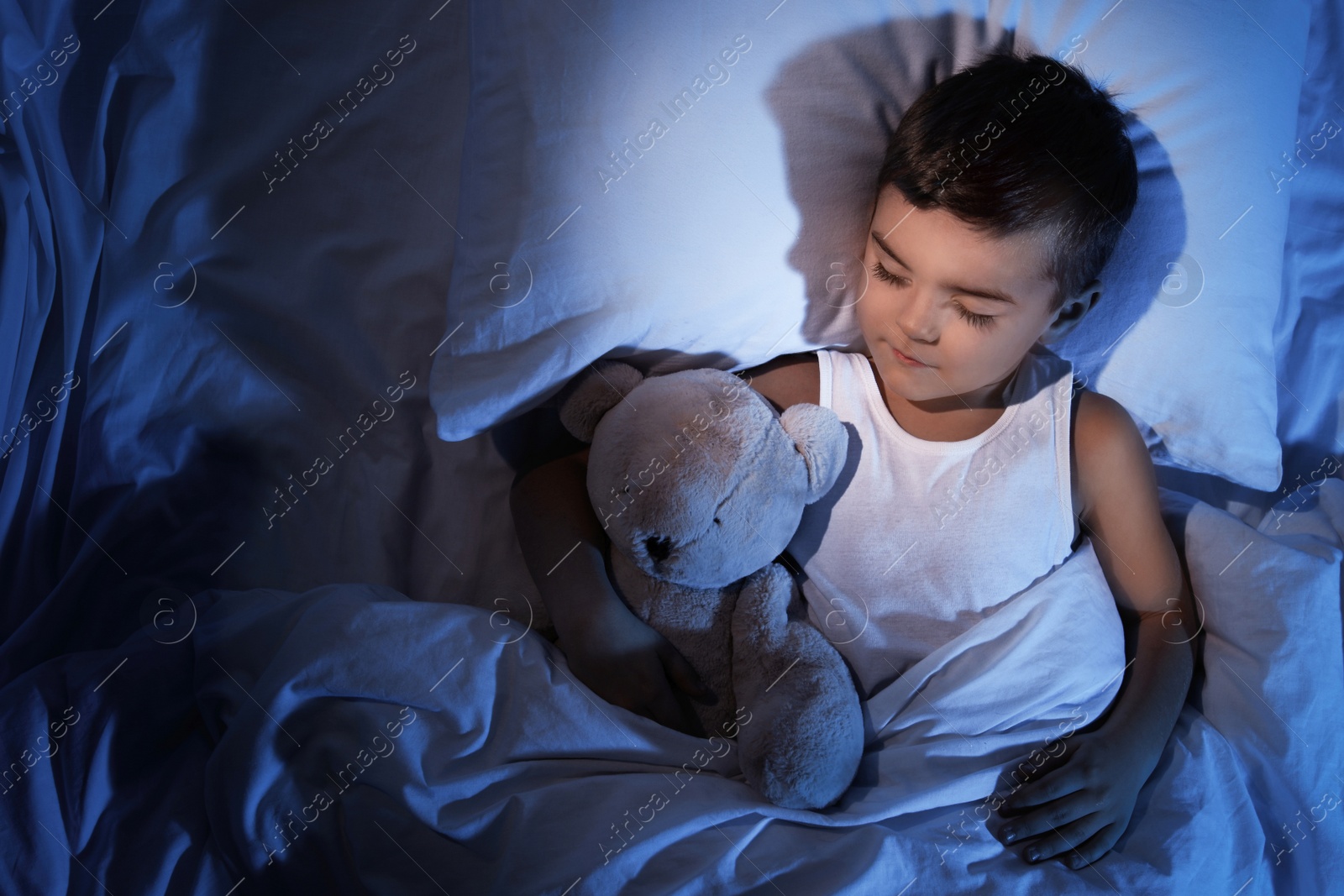 Photo of Little boy sleeping with teddy bear at home, top view. Bedtime