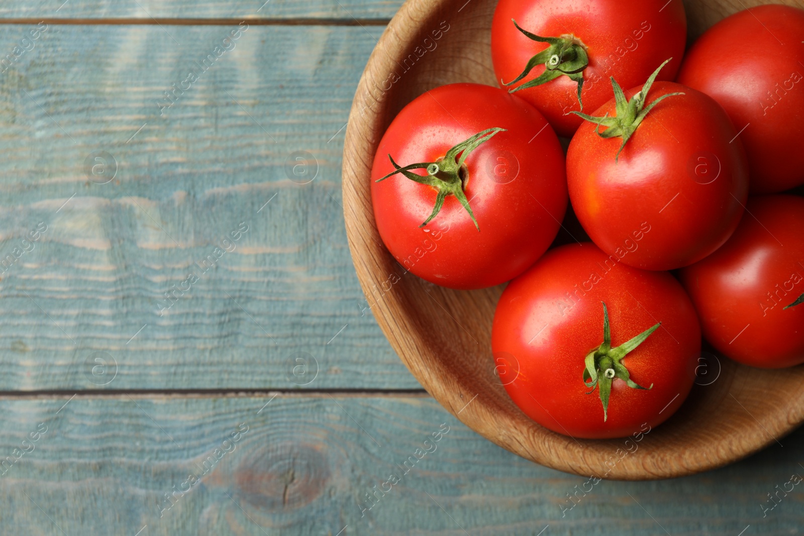 Photo of Ripe tomatoes in bowl on blue wooden table, top view. Space for text