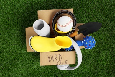 Photo of Phrase Yard Sale written on box with different stuff on green grass, top view