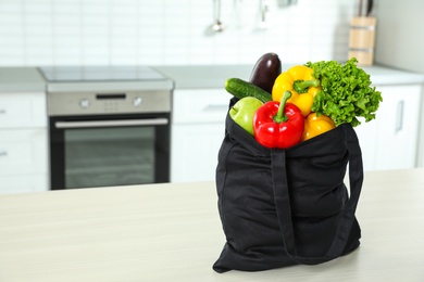 Photo of Textile shopping bag full of vegetables on table in kitchen. Space for text