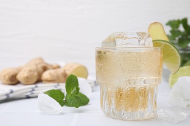 Photo of Glass of tasty ginger ale with ice cube and ingredients on white table, closeup. Space for text