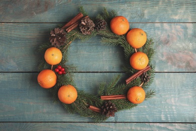 Photo of Decorative wreath with tangerines, fir tree branches and spices on wooden background, top view