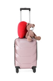 Photo of Red travel pillow and toy bear on suitcase against white background