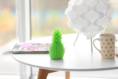 Stylish pineapple candle and cup of coffee on table indoors. Home decorating idea