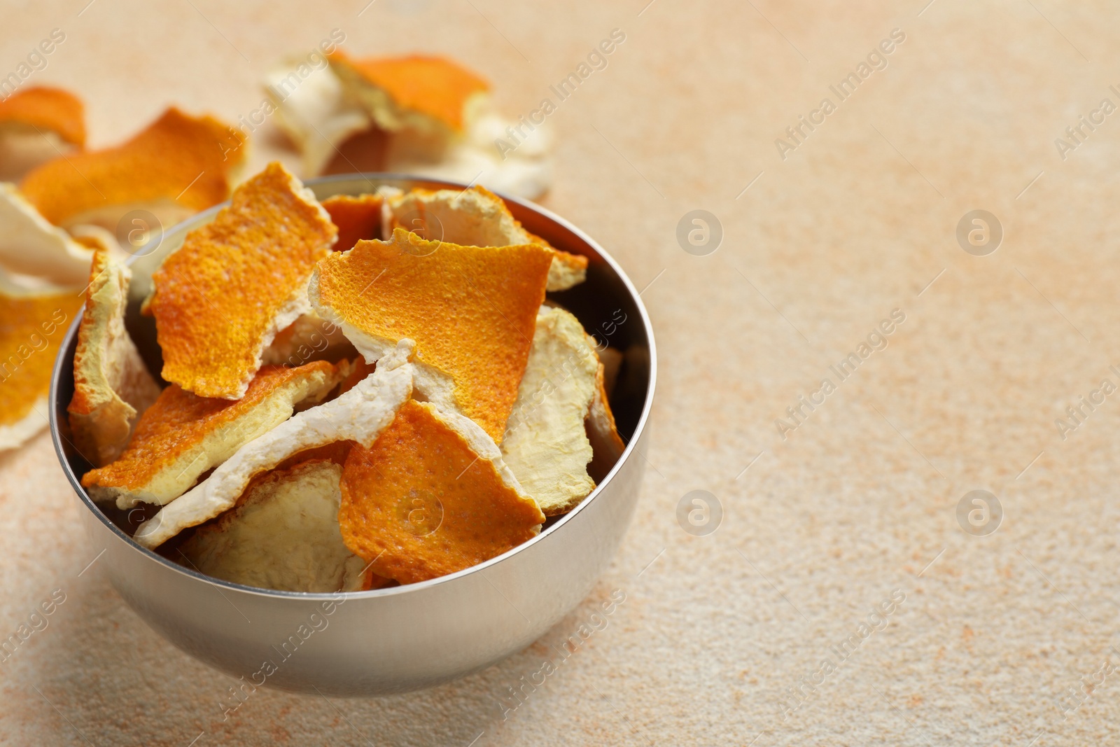 Photo of Dry orange peels in bowl on beige table, space for text