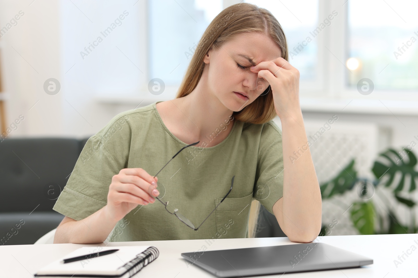 Photo of Overwhelmed young woman sitting with laptop at table in room