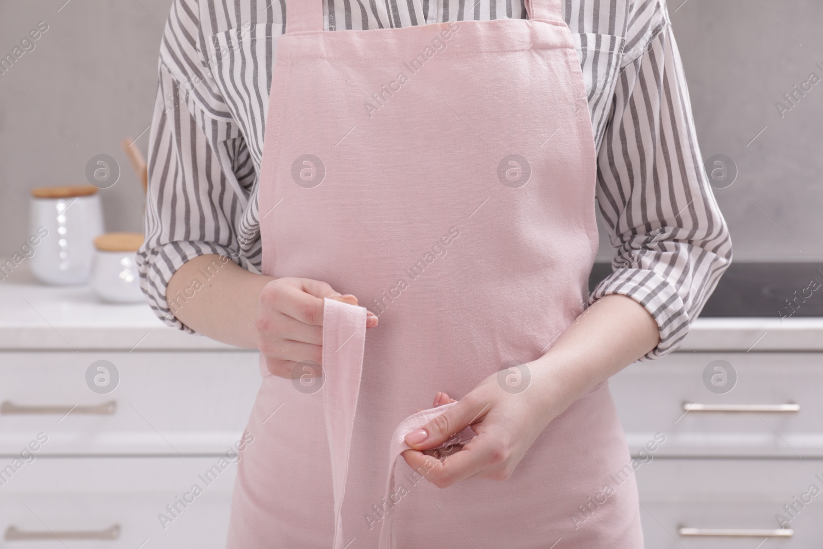 Photo of Woman putting on pink apron in kitchen , closeup