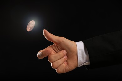 Image of Man throwing coin on black background, closeup. Making decision