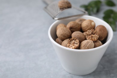 Photo of Nutmegs in bowl on light grey table, closeup. Space for text