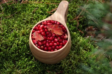 Many tasty ripe lingonberries and autumn leaves in wooden cup outdoors, above view