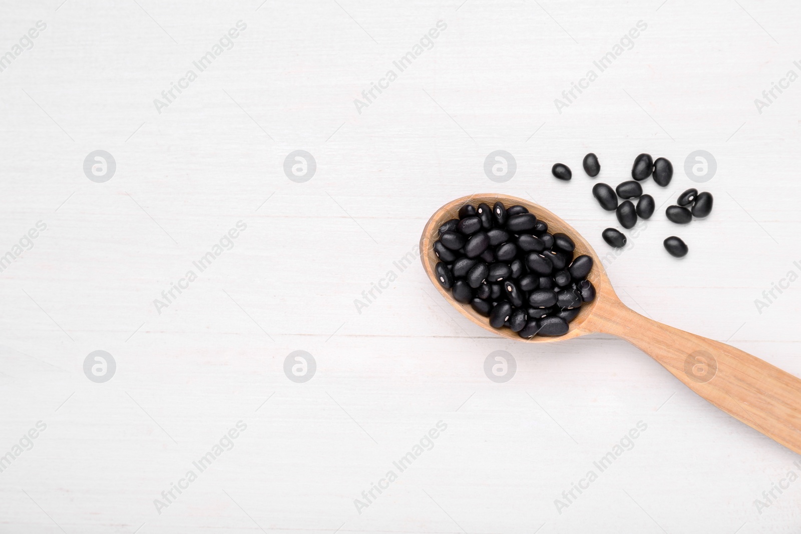 Photo of Spoon of raw black beans on white wooden table, top view. Space for text