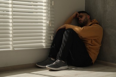 Sad man sitting on floor near window. Space for text