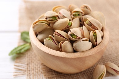 Photo of Tasty pistachios in bowl on white wooden table, closeup