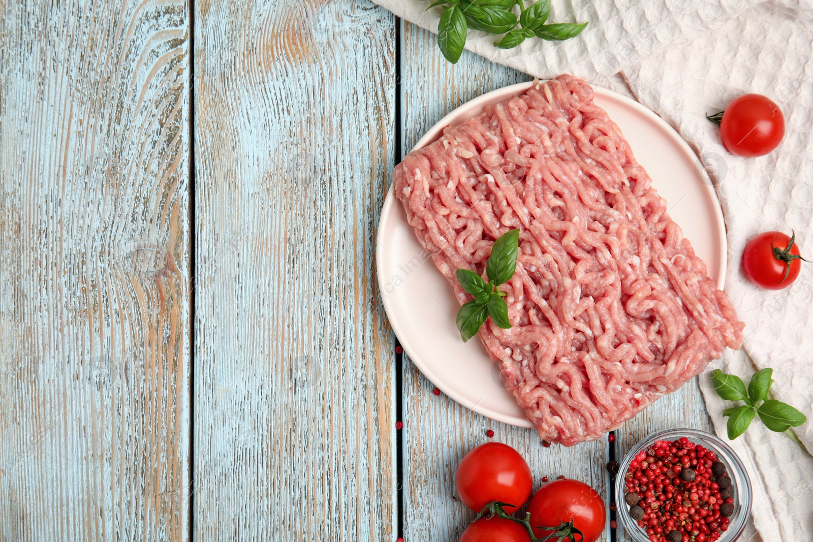 Photo of Raw chicken minced meat with basil, spices and tomatoes on light blue wooden table, flat lay. Space for text