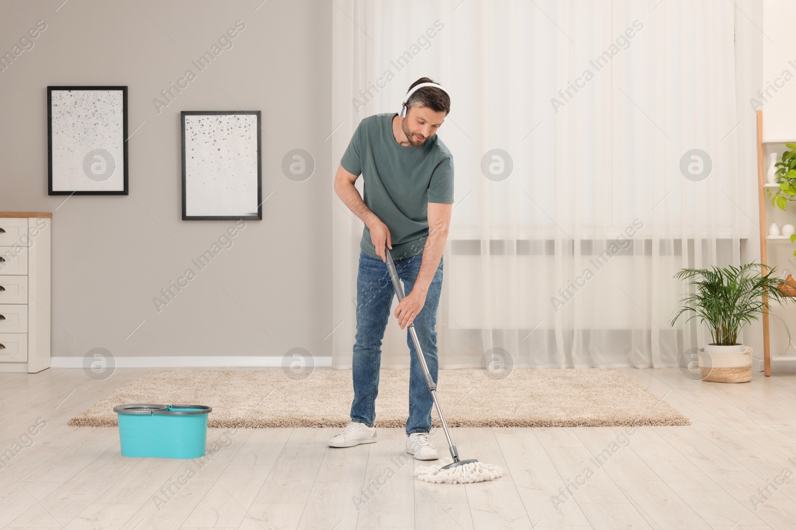 Photo of Enjoying cleaning. Man in headphones listening to music and mopping floor at home