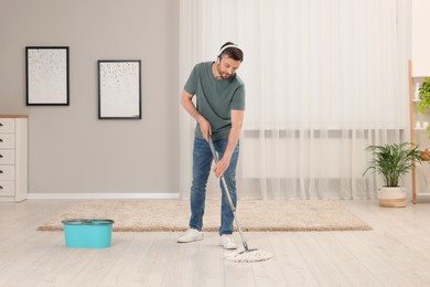 Enjoying cleaning. Man in headphones listening to music and mopping floor at home