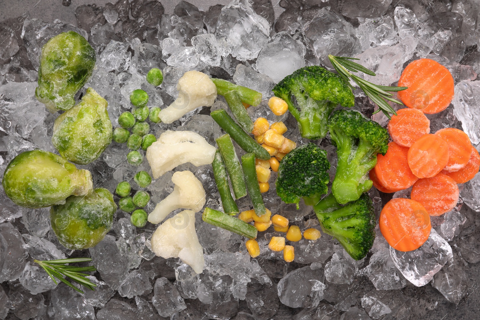 Photo of Different frozen vegetables with ice on grey table, flat lay