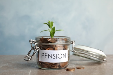 Photo of Glass jar with label PENSION, coins and green plant on marble table