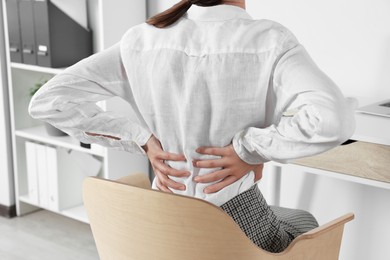 Woman suffering from back pain while sitting in office, closeup. Symptom of scoliosis