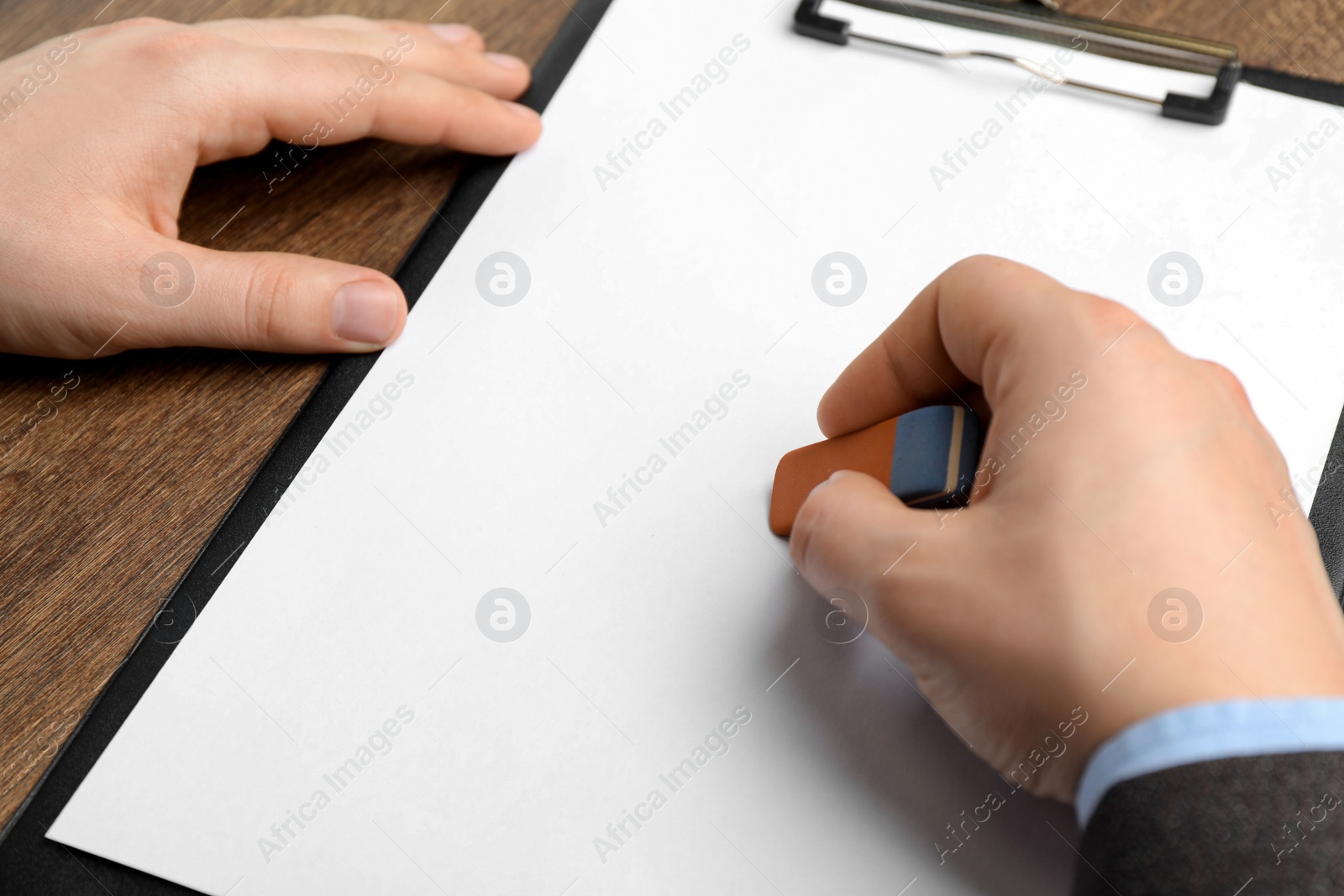 Photo of Man erasing something on paper at wooden table, closeup