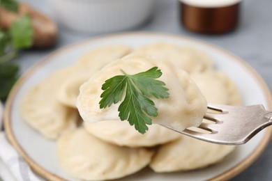 Photo of Fork with delicious dumpling (varenyk) with tasty filling and parsley above plate, closeup