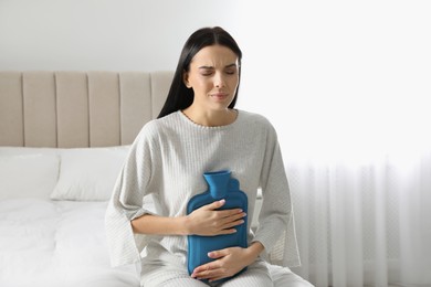 Photo of Woman using hot water bottle to relieve abdominal pain on bed at home