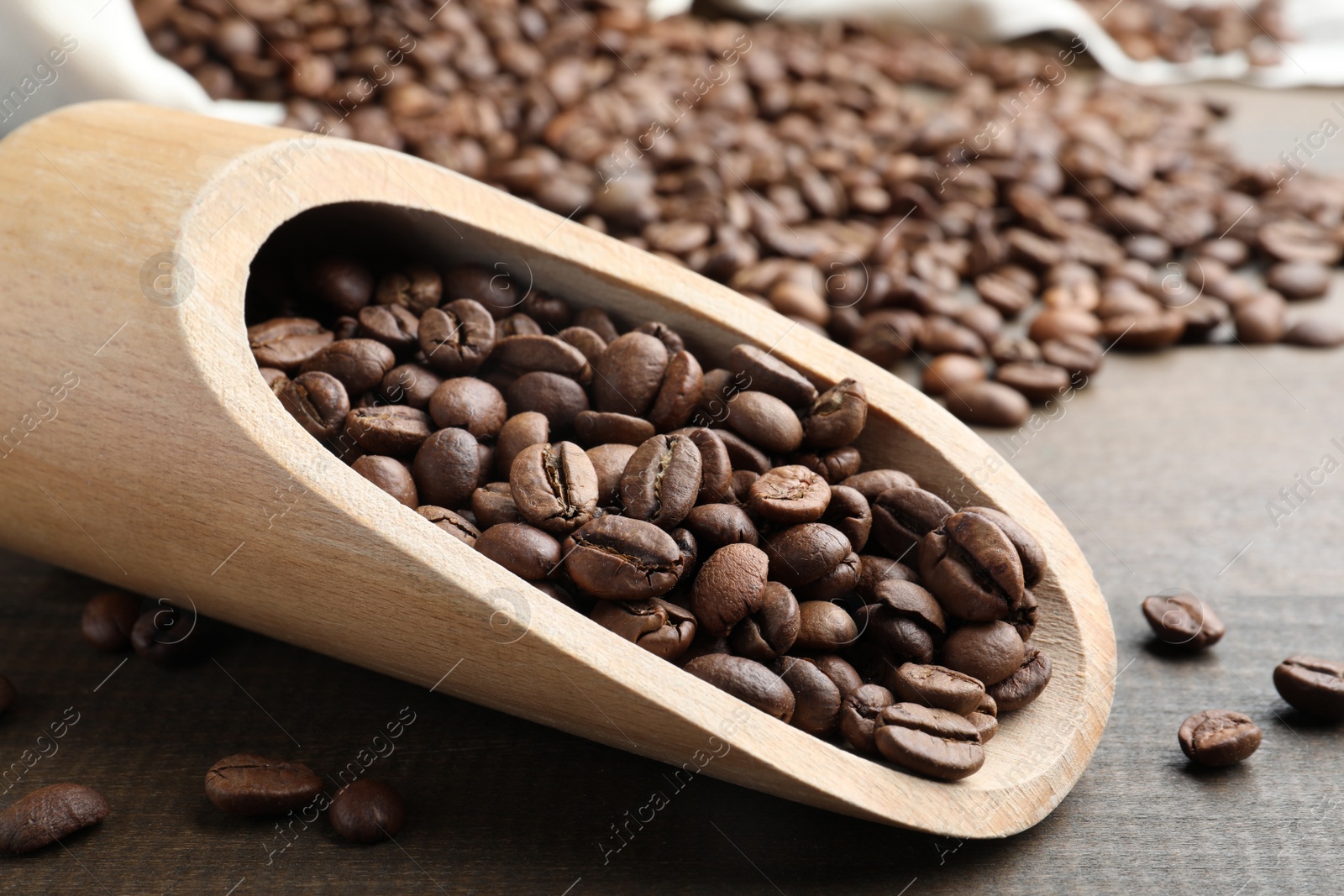 Photo of Scoop with roasted coffee beans on wooden table, closeup