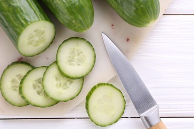 Photo of Cucumbers, knife and marble cutting board on white wooden table, top view