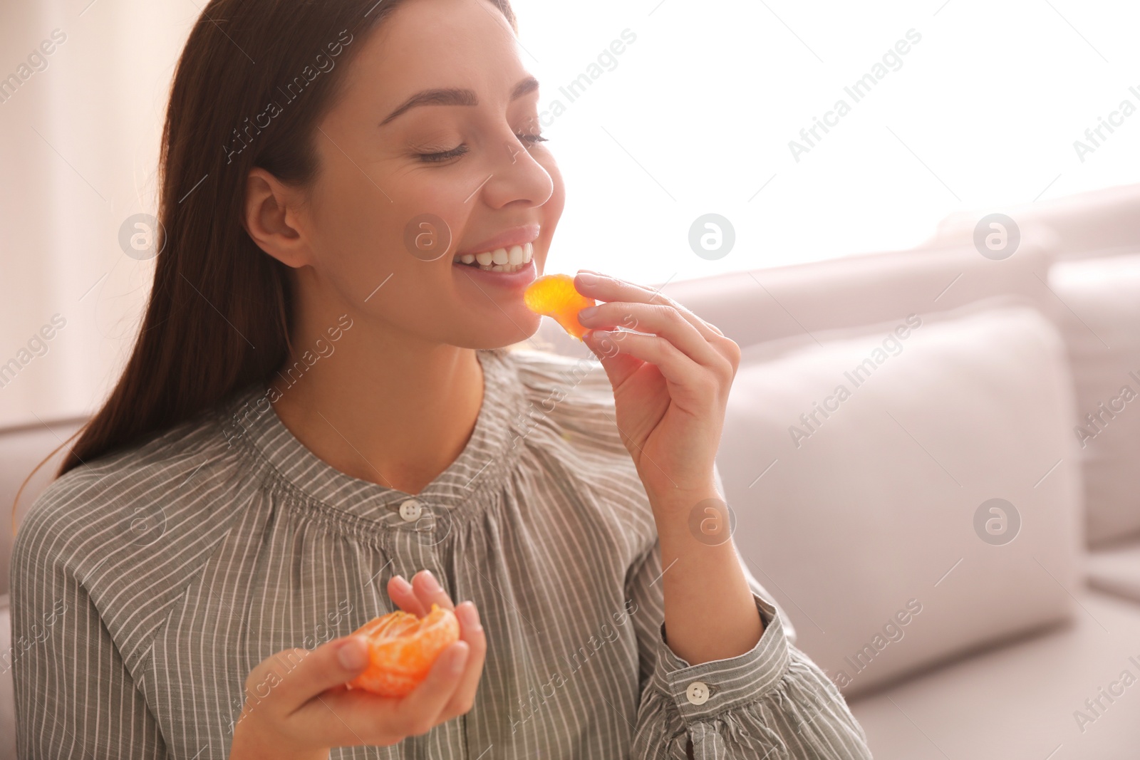 Photo of Happy woman eating tasty fresh tangerine indoors