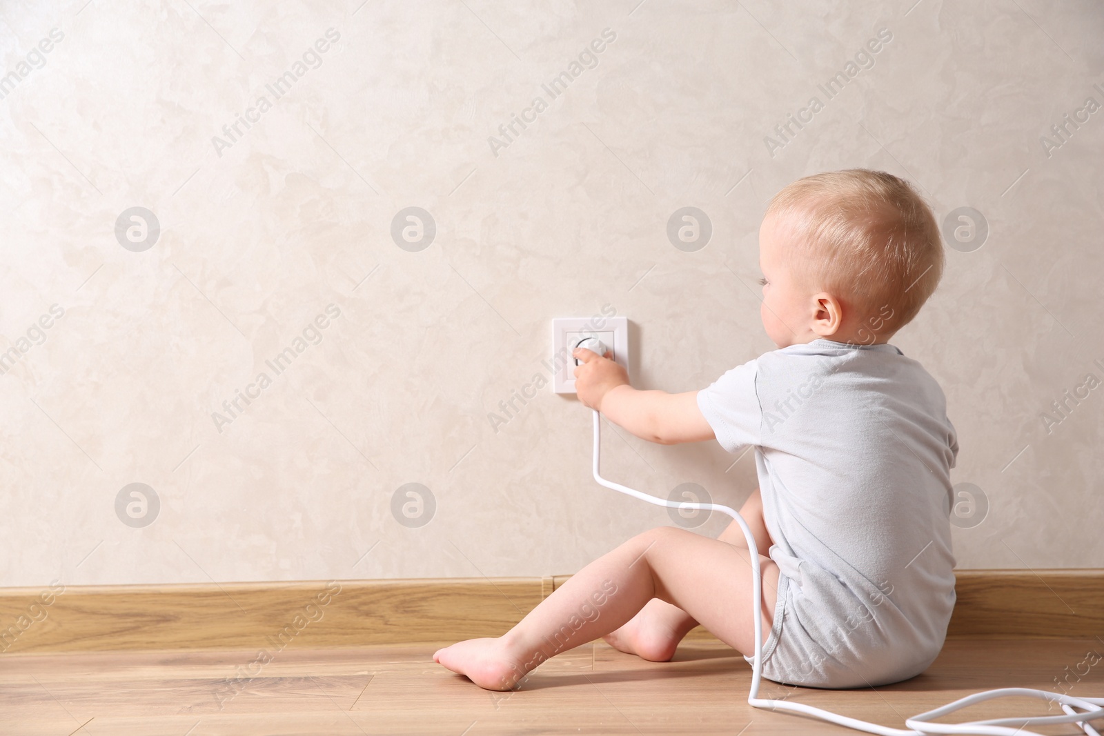 Photo of Little child playing with electrical socket and plug indoors, space for text. Dangerous situation