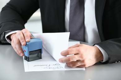 Male notary stamping document at table, closeup