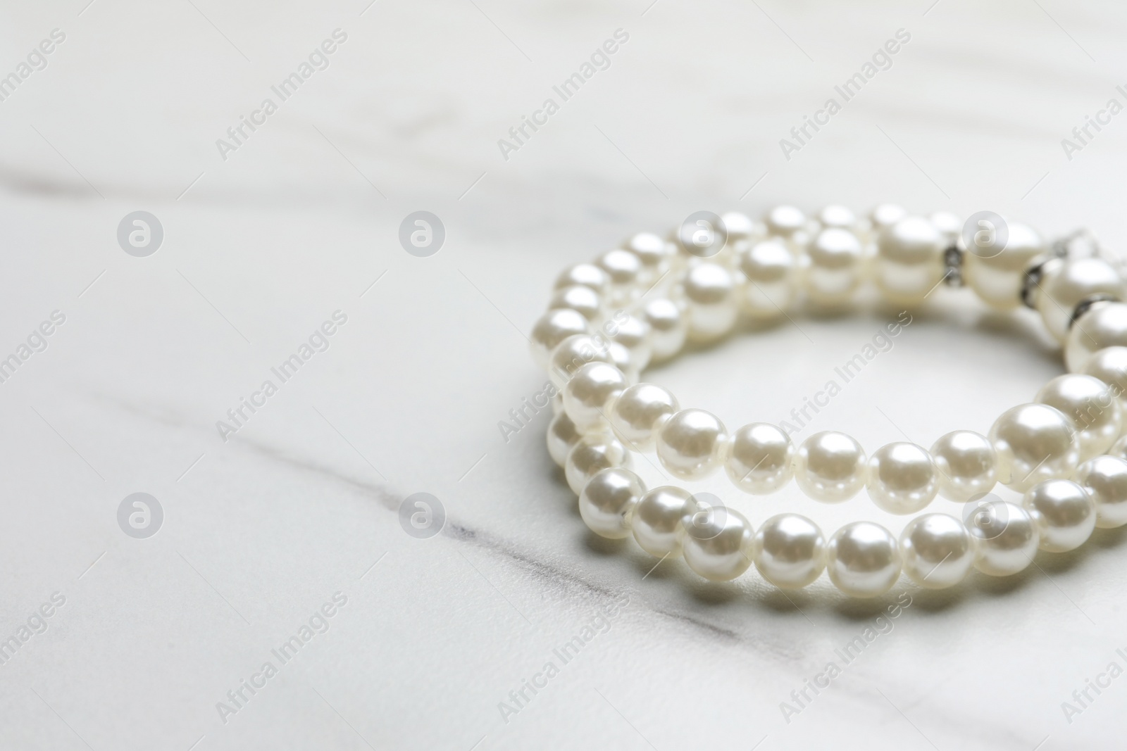 Photo of Elegant pearl bracelets on white marble table, closeup. Space for text