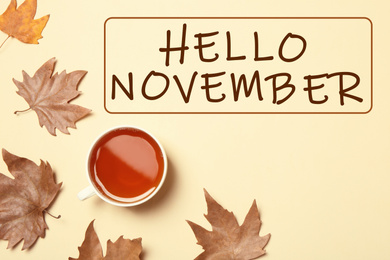 Text Hello November, cup of tea and autumn leaves on beige background, top view