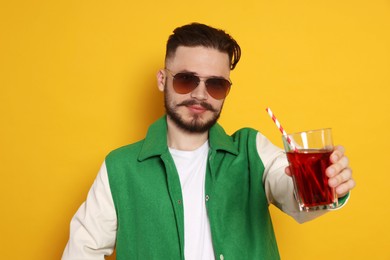 Handsome young man with glass of juice on yellow background