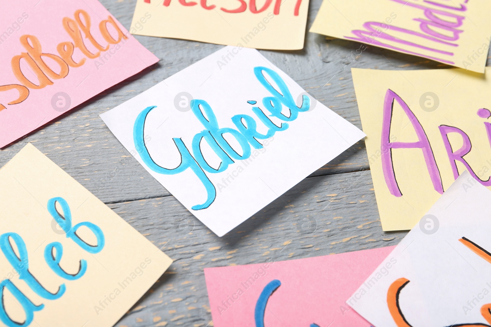 Photo of Colorful paper sheets with written different baby names on grey wooden table, closeup