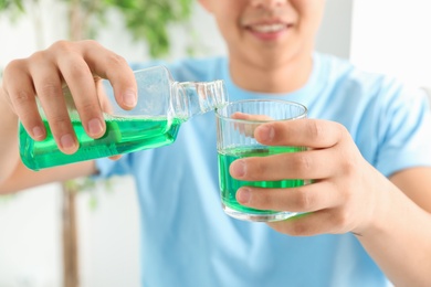 Photo of Man pouring mouthwash from bottle into glass, closeup. Teeth care