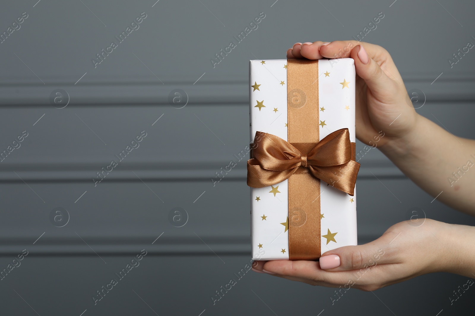 Photo of Woman holding gift box near grey wall, closeup. Space for text