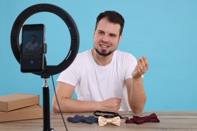 Smiling fashion blogger showing bow ties while recording video at table against light blue background