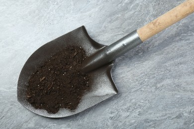Photo of Metal shovel with fertile soil on gray textured surface, top view