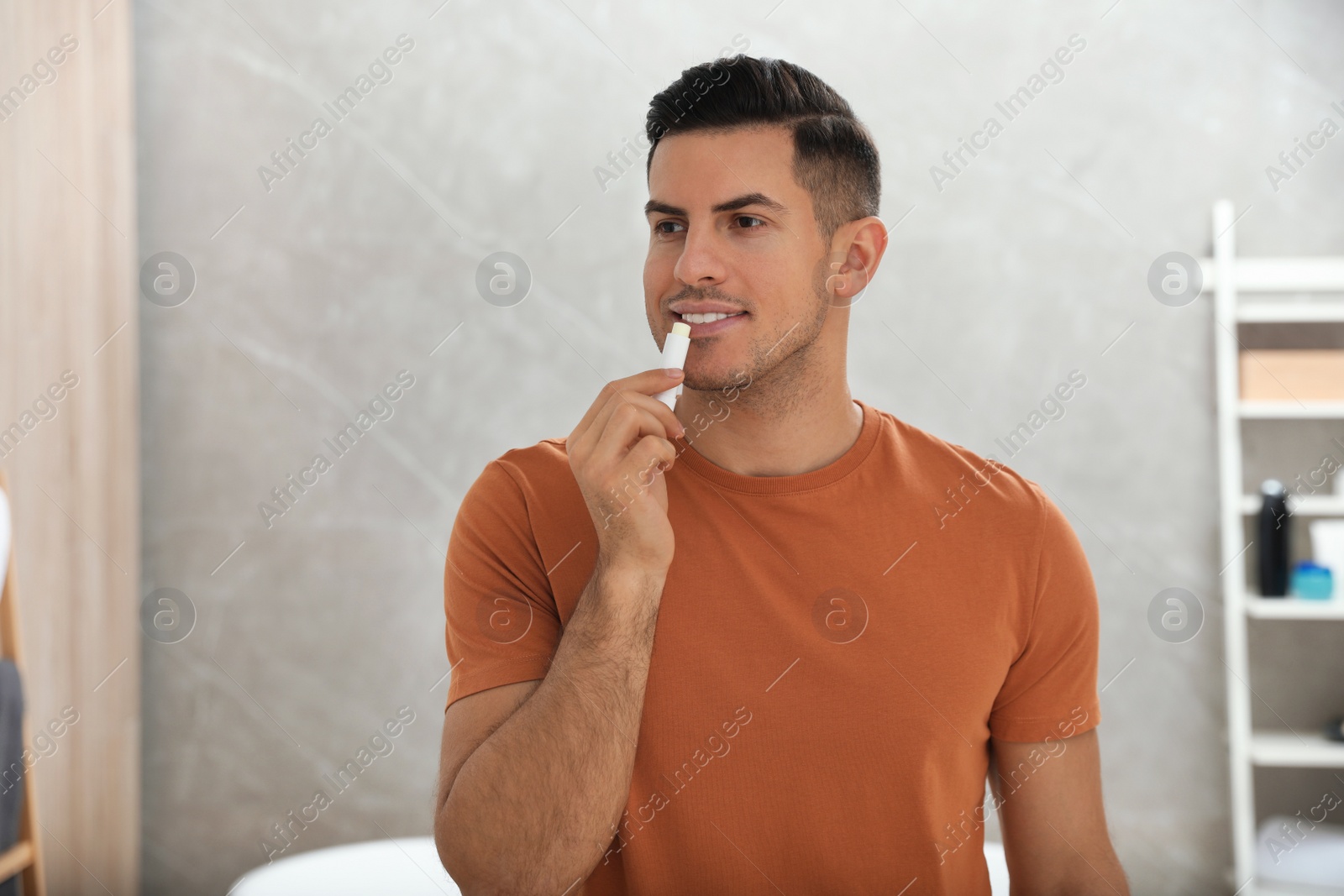 Photo of Man applying hygienic lip balm in bathroom