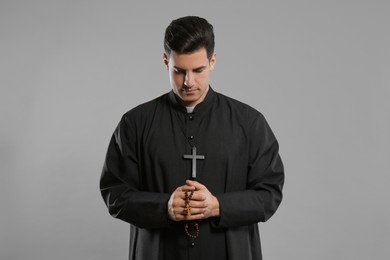 Photo of Priest with rosary beads praying on grey background