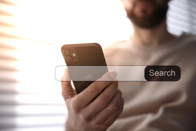Image of Search bar of website near smartphone. Man using device indoors, closeup