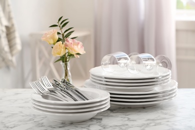 Set with clean dishes and vase of flowers on white marble table