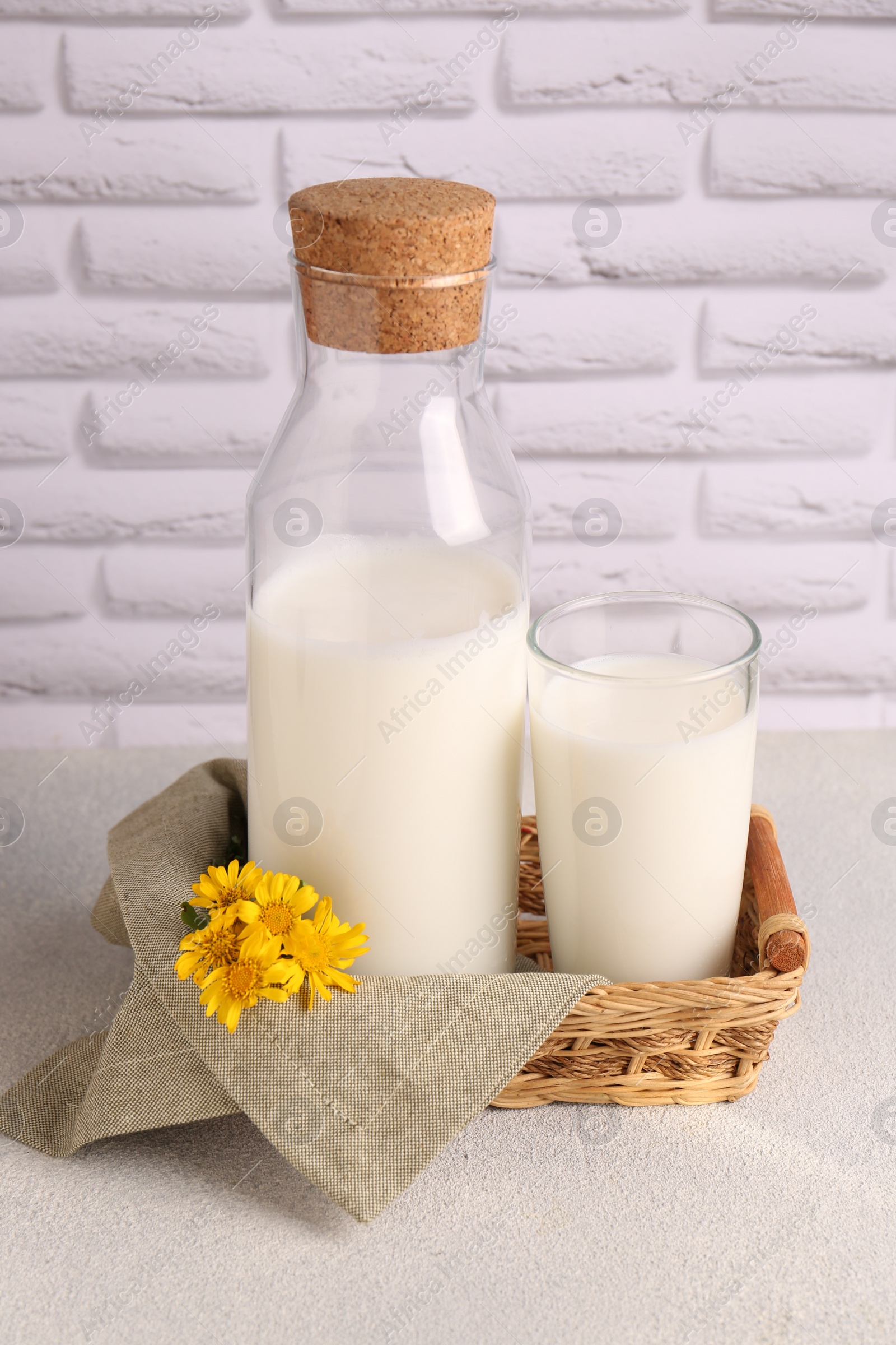 Photo of Glass and bottle of fresh milk on table against white brick wall