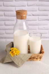 Photo of Glass and bottle of fresh milk on table against white brick wall